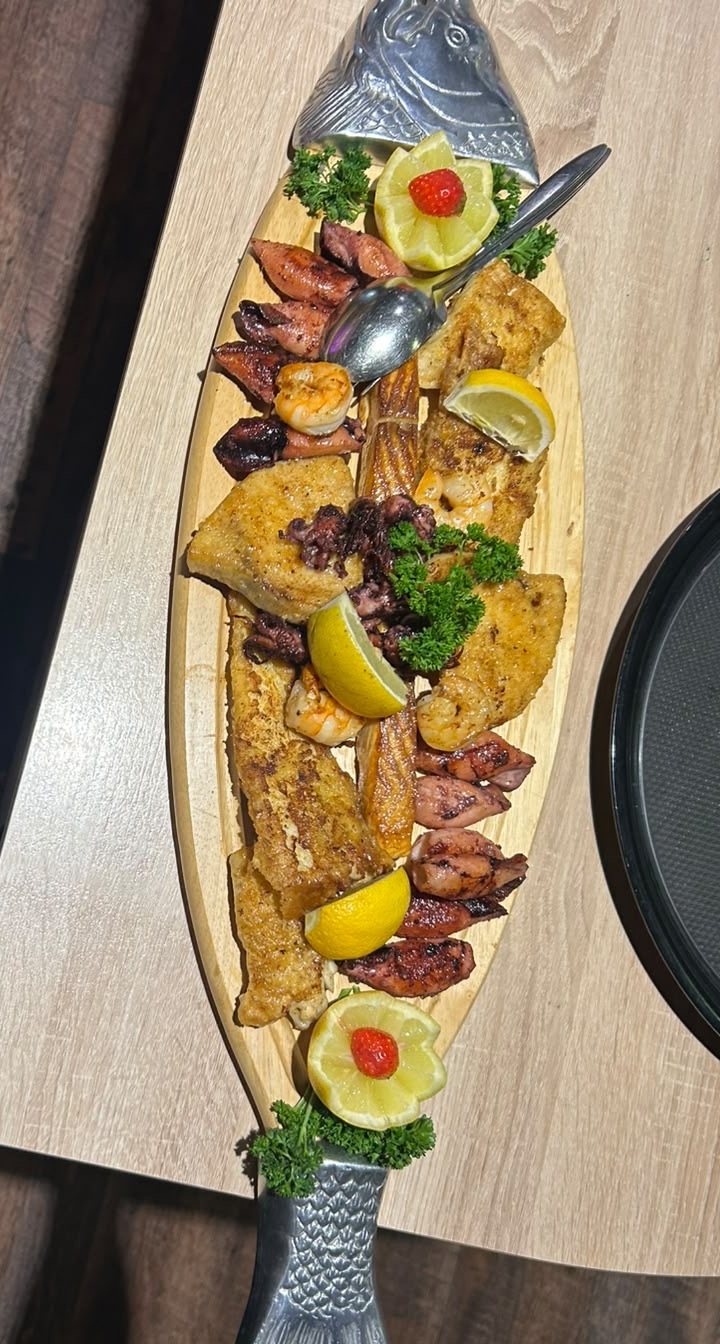 Fischplatte mit Filets, Garnelen, Zitrone und Petersilie auf einer Servierplatte in Fischform