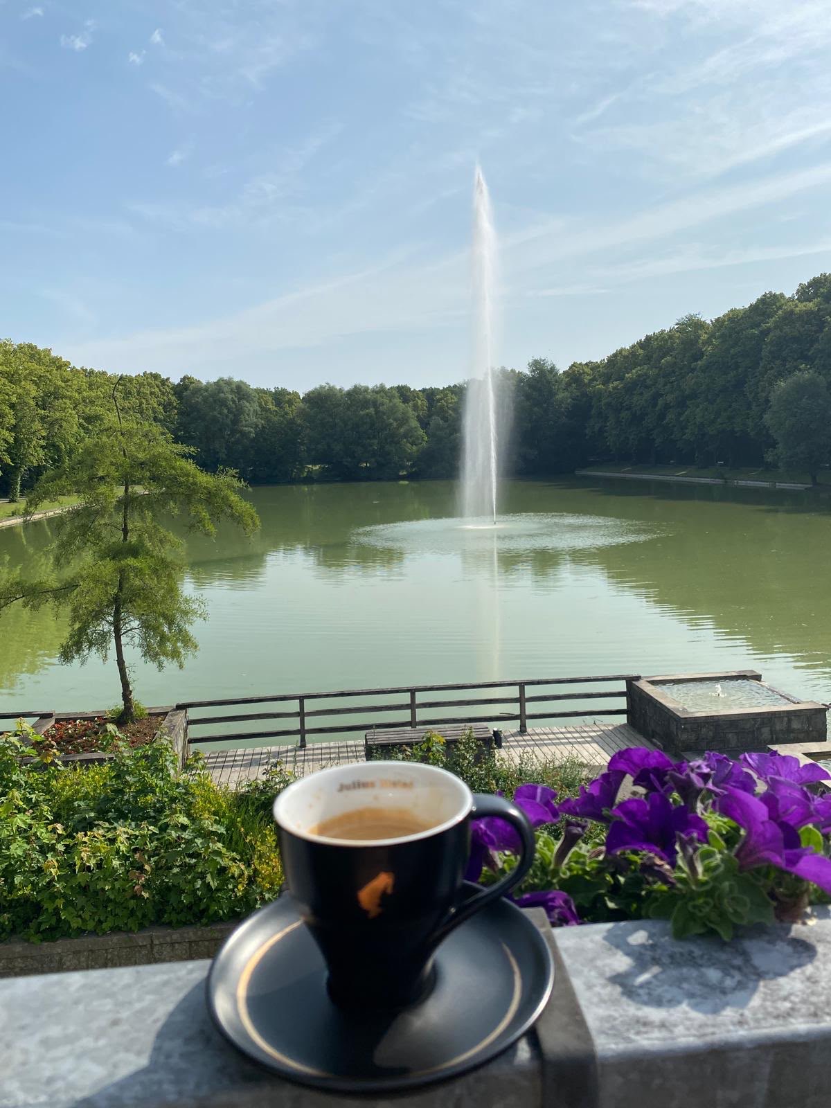 Eine Tasse Kaffee auf der Terrassenbrüstung mit Blick auf den Teich und die Fontäne