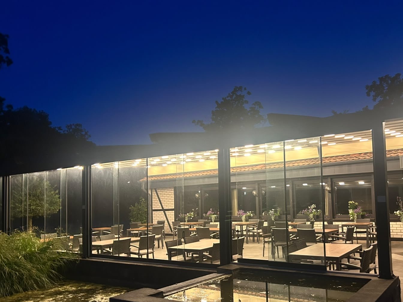 Die überdachte Terrasse am Abend, warm beleuchtet, davor das Wasserbecken